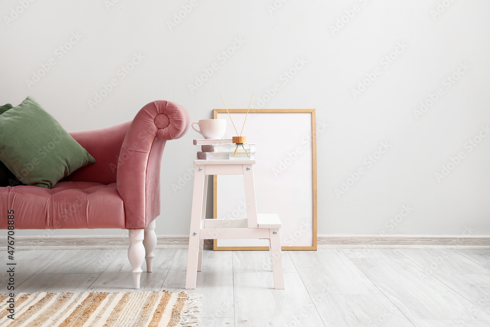 Stepladder with cup, books, reed diffuser, frame and armchair near light wall