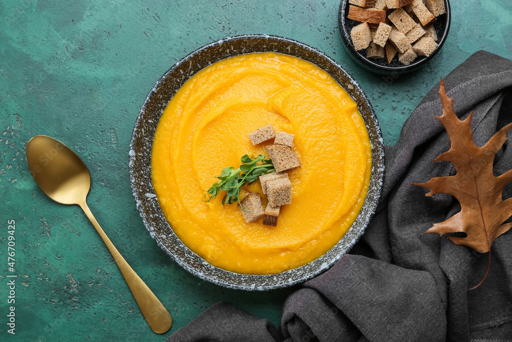 Bowl of tasty pumpkin cream soup and bread on green background