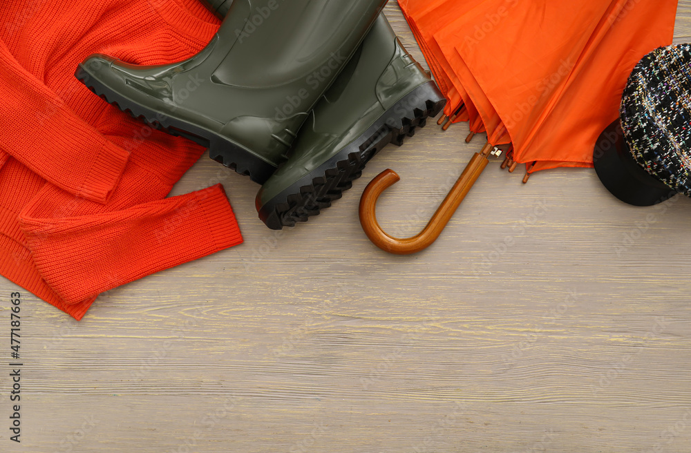 Umbrella, rubber boots, sweater and cap on grey wooden background, closeup