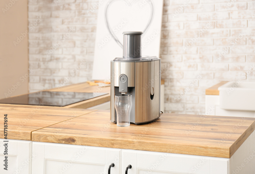 Modern juicer with glass on table in kitchen