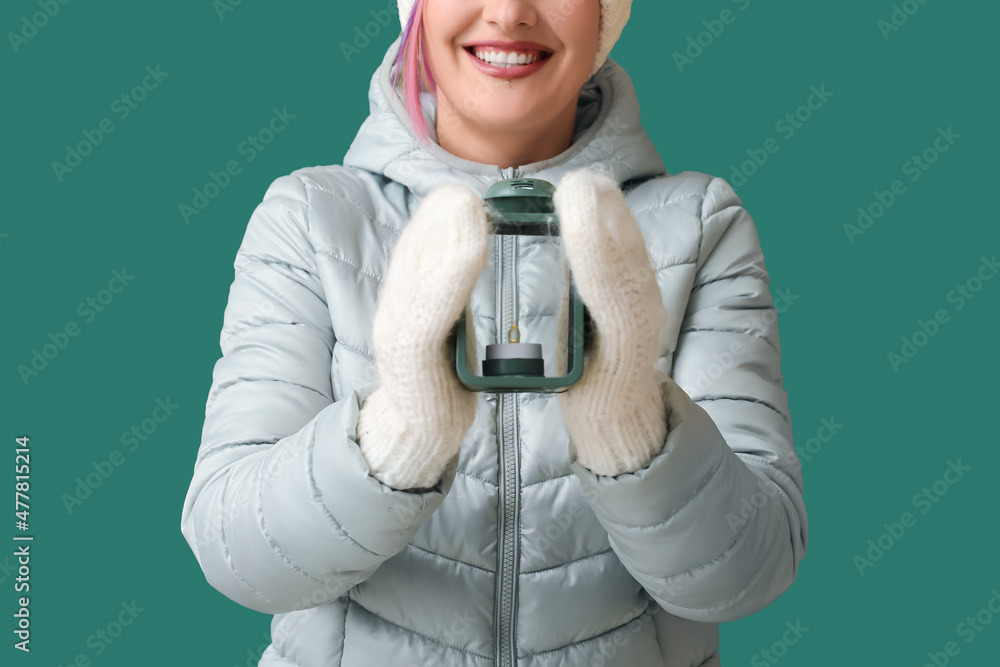 Woman in winter clothes and with lantern on color background