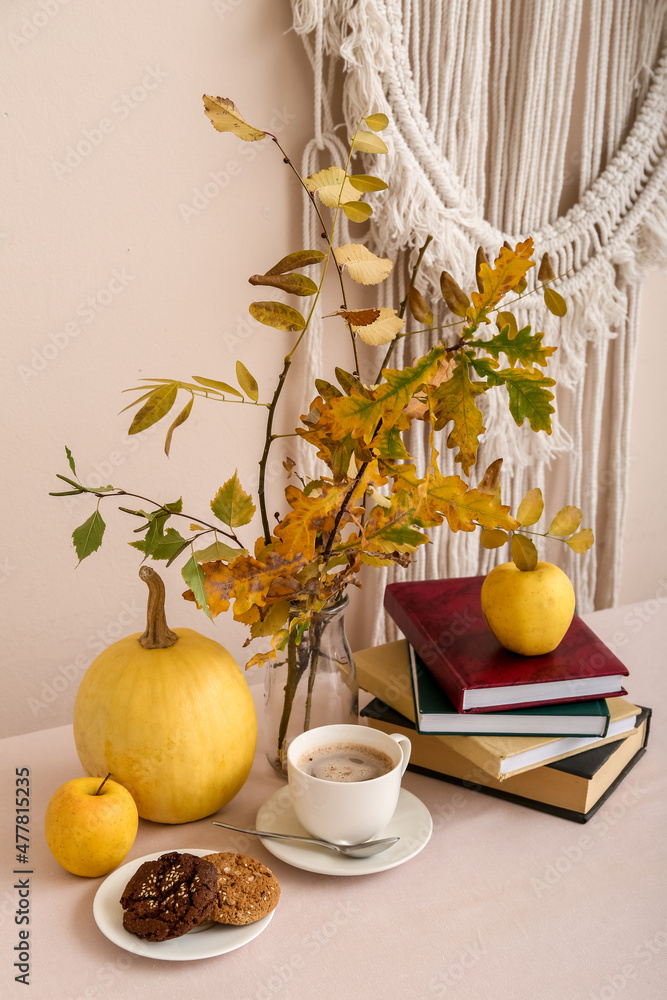 Composition with autumn branches, pumpkin, stack of books, cup of coffee and plate with cookies on t