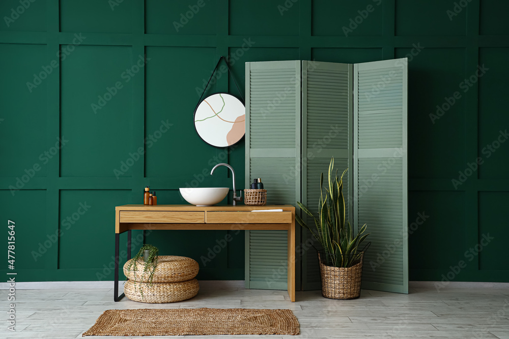 Interior of stylish bathroom with sink, mirror and green folding screen