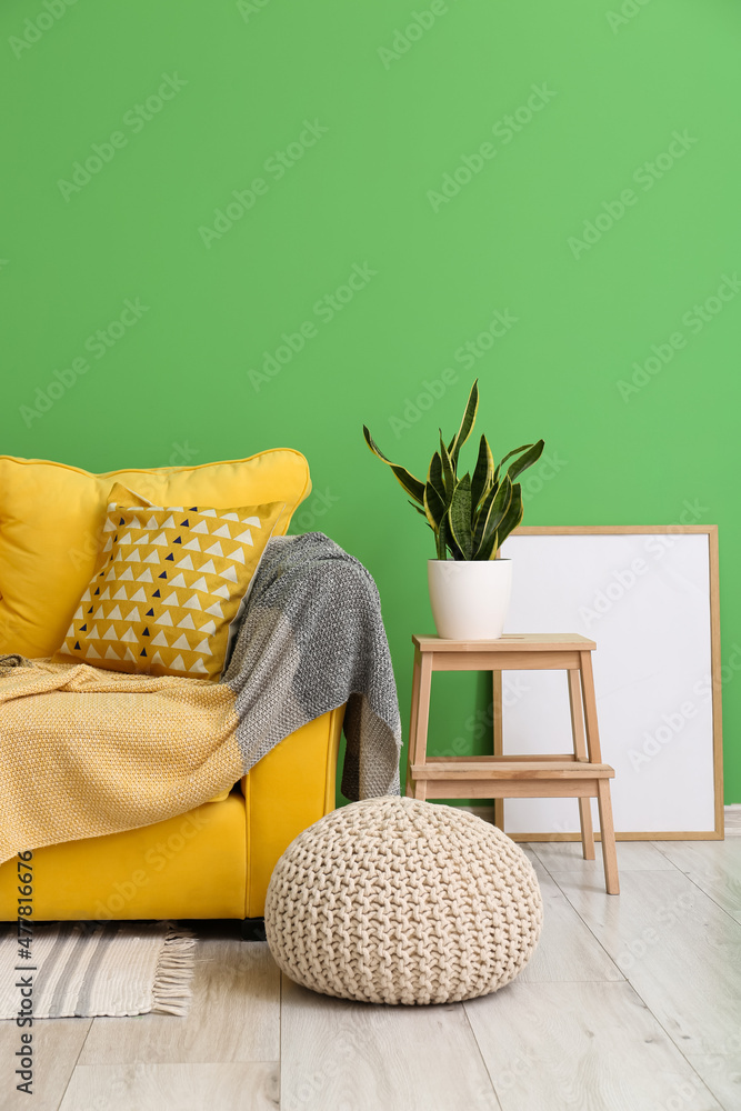 Cozy sofa, pouf, step stool with houseplant and frame near green wall