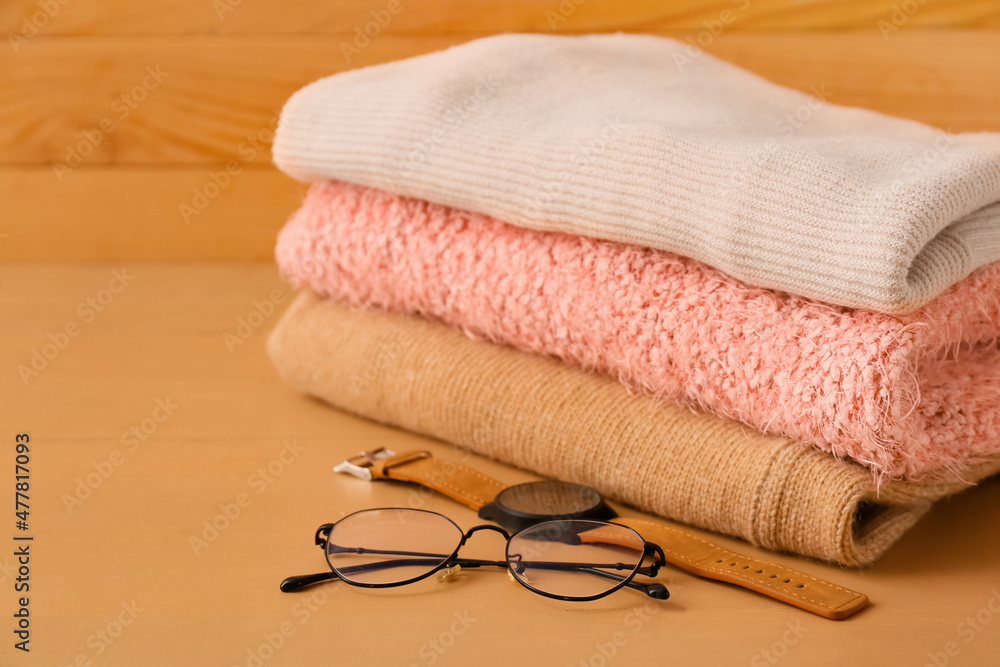 Stack of different cozy sweaters, eyeglasses and wristwatch on wooden background