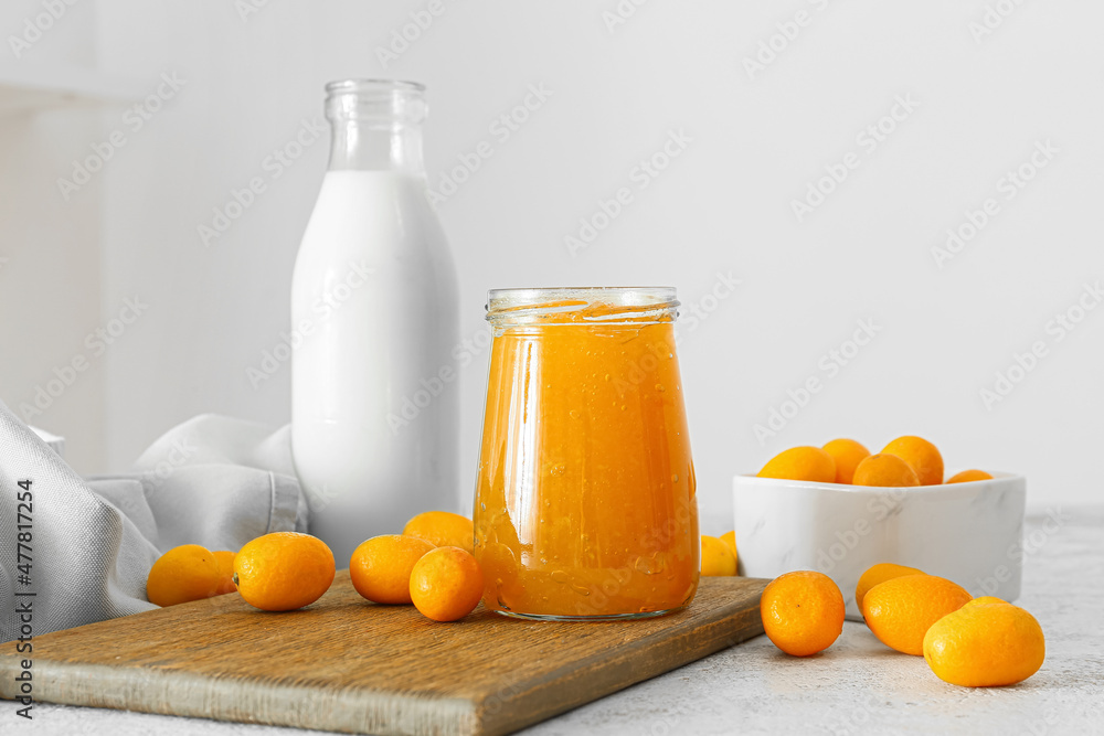 Jar of tasty kumquat jam and fresh fruits on light background