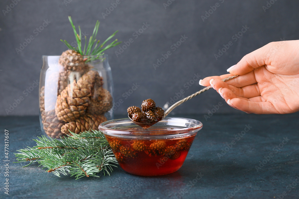 Woman with tasty pine cone jam on dark background