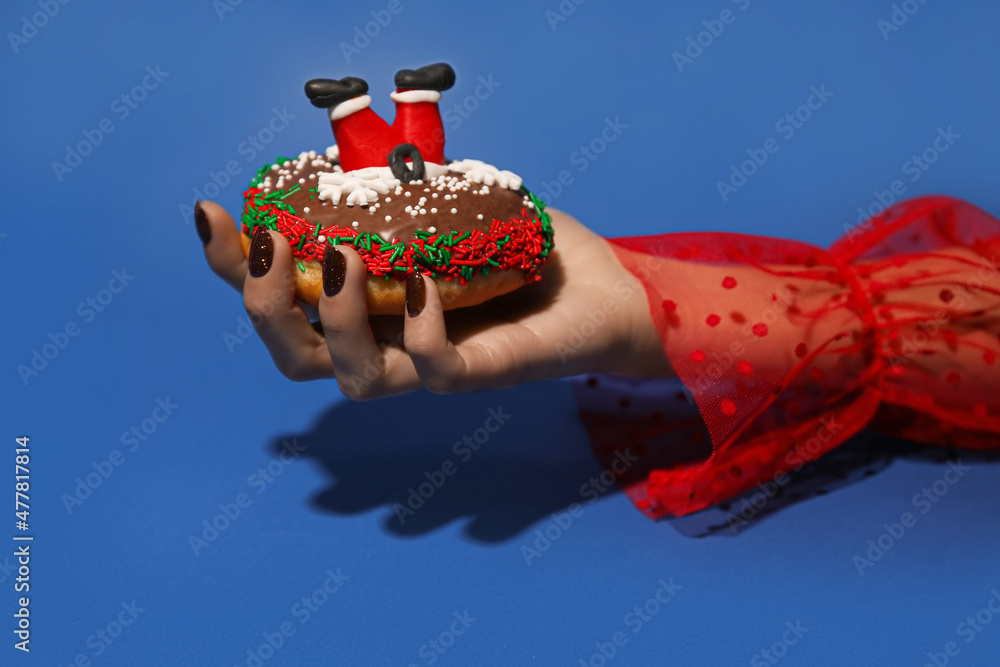 Woman holding tasty Christmas donut on blue background