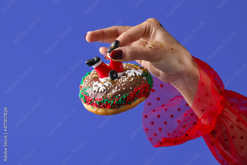 Woman holding tasty Christmas donut on blue background