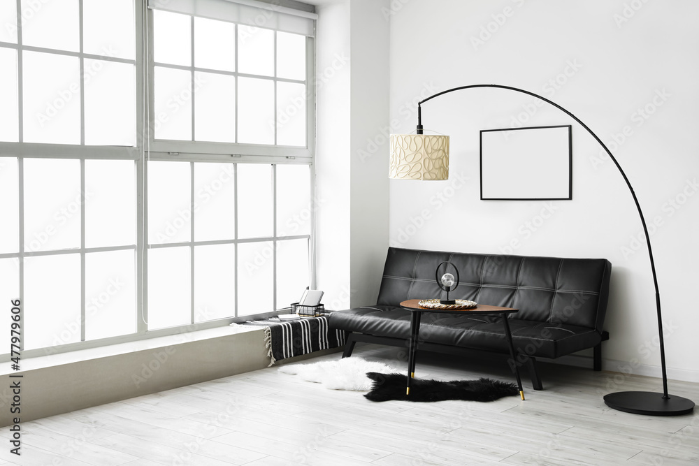 Interior of light living room with black couch, table and lamps