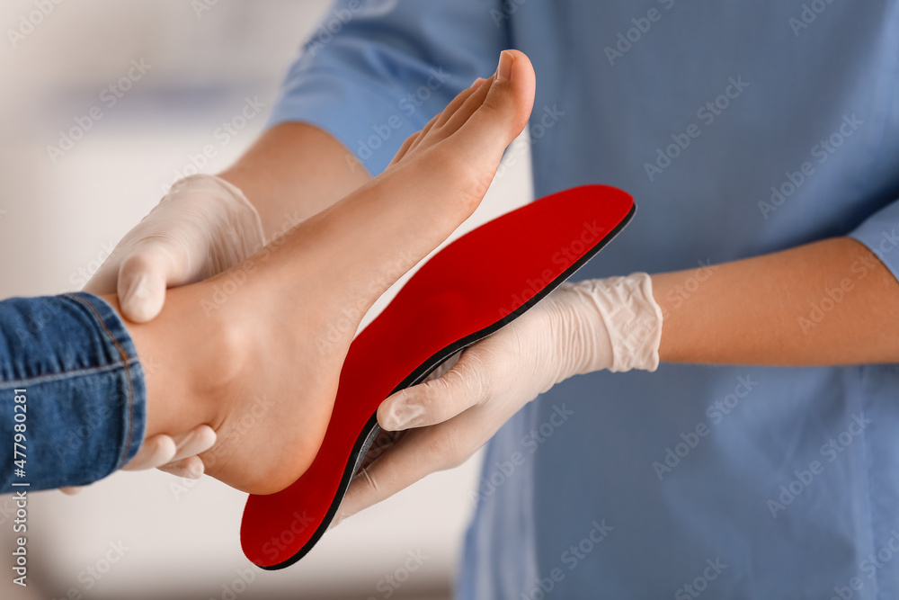 Female orthopedist fitting red insole on patients foot in clinic, closeup