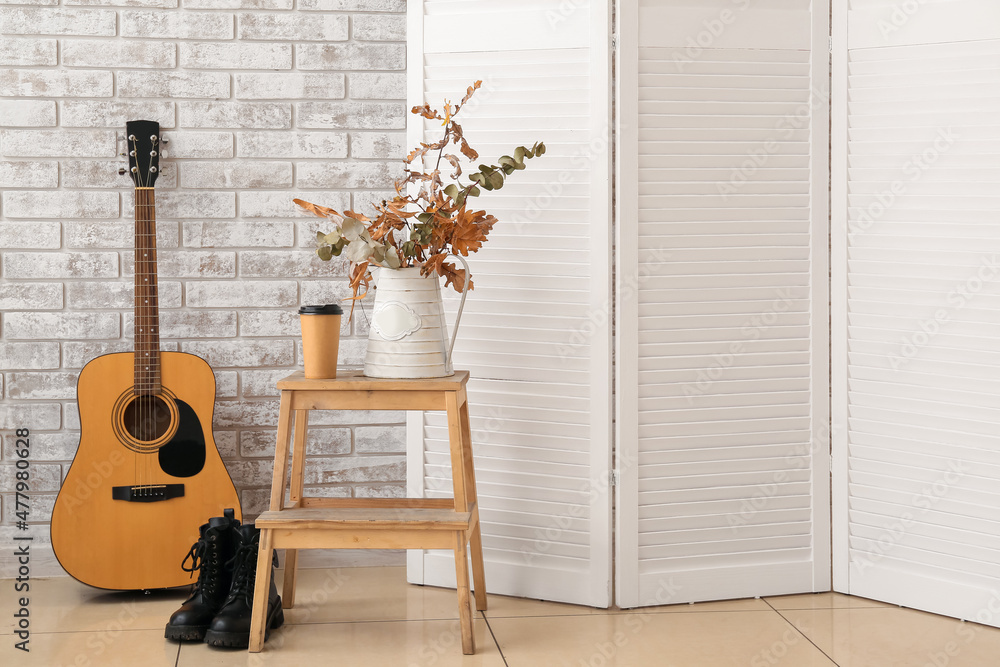 Stepladder stool with autumn decor, shoes and guitar near light brick wall