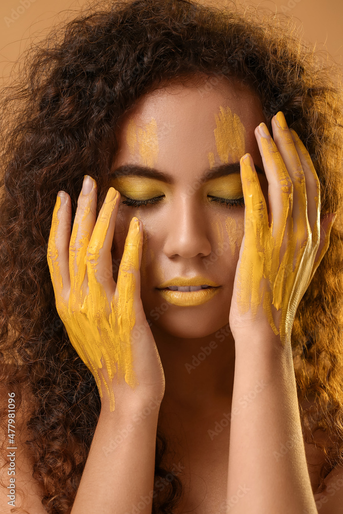 Beautiful young woman with yellow paint on her face and body against color background