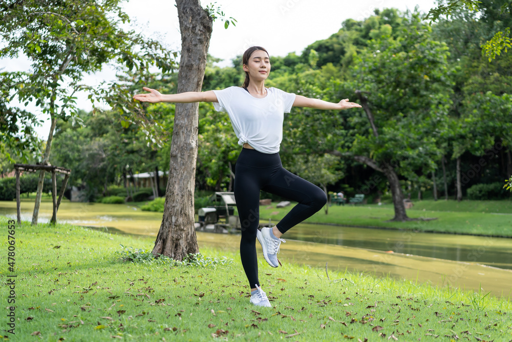 亚洲年轻运动女性在公园锻炼前伸展身体热身。