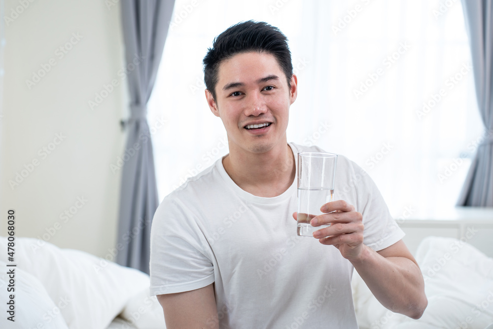 Portrait of Asian active strong man holding clean water in bedroom.