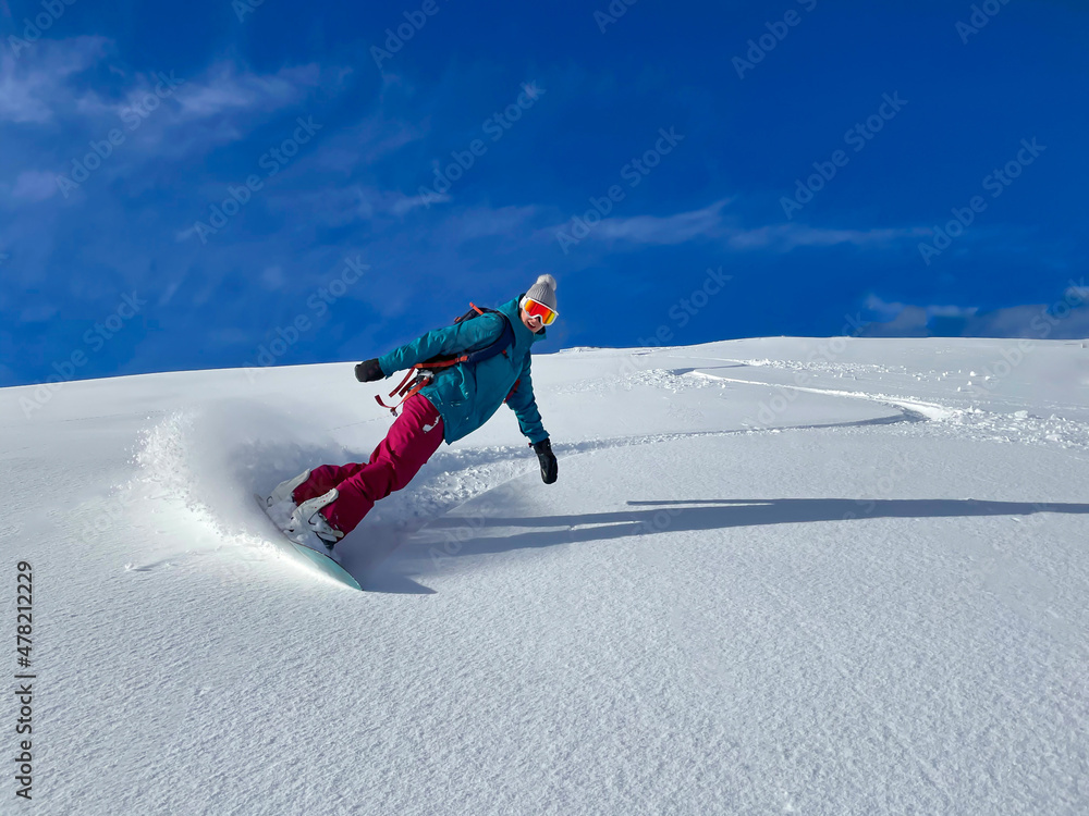 兴高采烈的女单板滑雪运动员在滑雪道上骑行时喷洒新鲜的粉末雪。