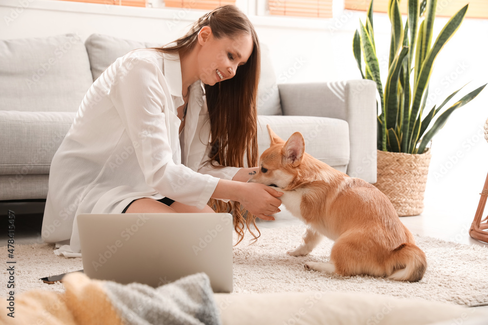 家里地板上坐着可爱的柯基犬的年轻女人