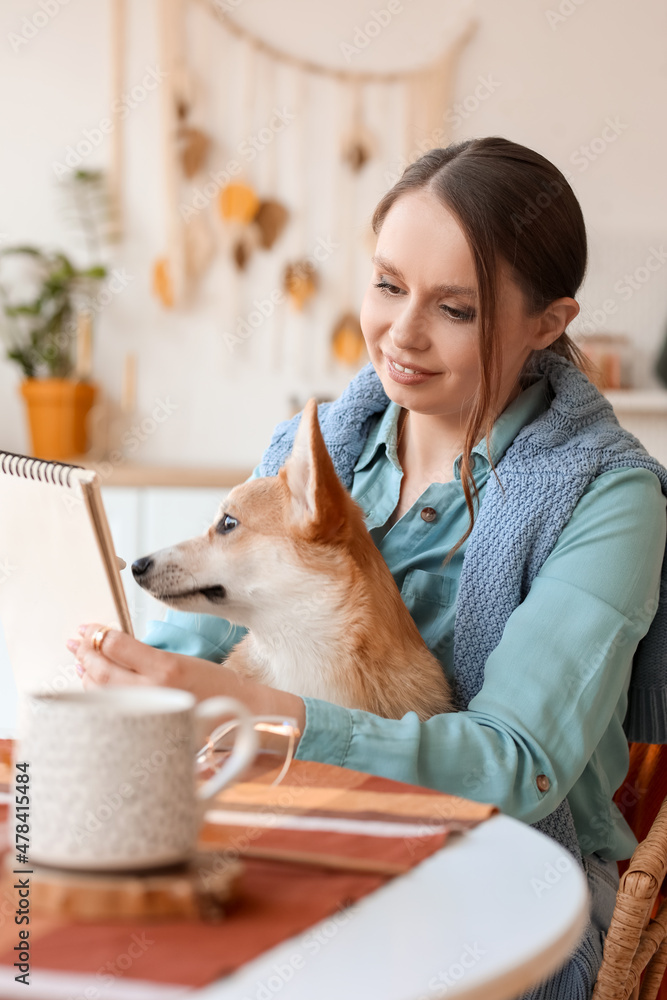 年轻女子带着可爱的柯基犬和笔记本坐在厨房的桌子旁