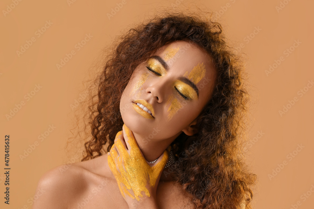 Beautiful young woman with yellow paint on her face and body against color background