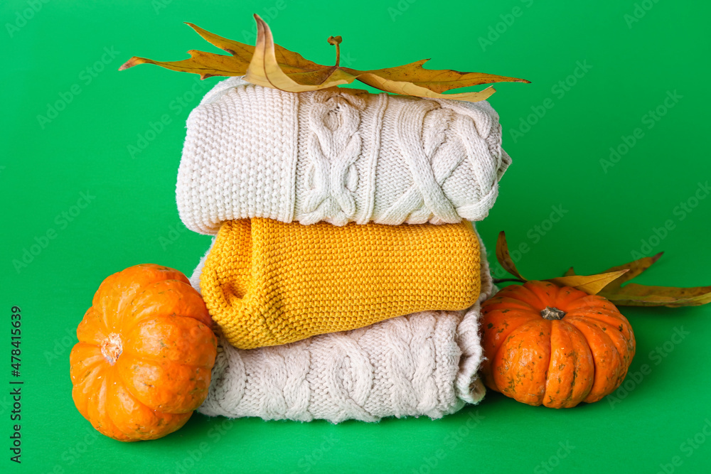 Stack of baby clothes, pumpkins and leaves on color background