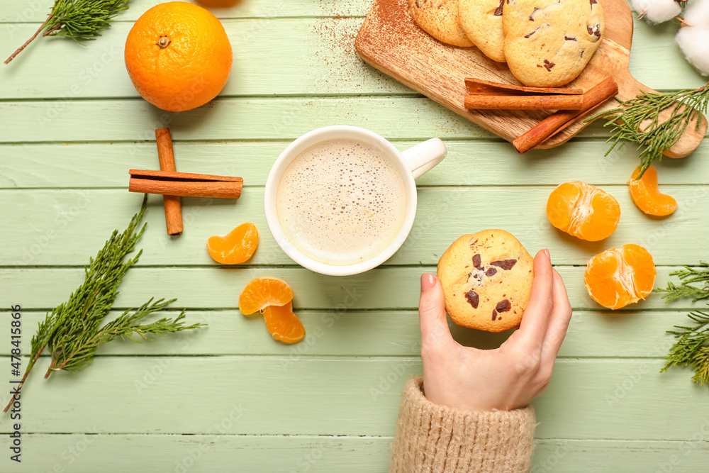 Female hand with cookie, cup of cacao and tangerines on color wooden background. Hello winter