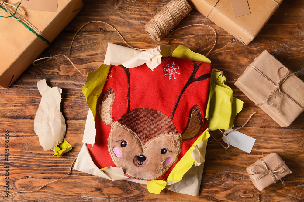 Torn Christmas present with sweater on wooden background