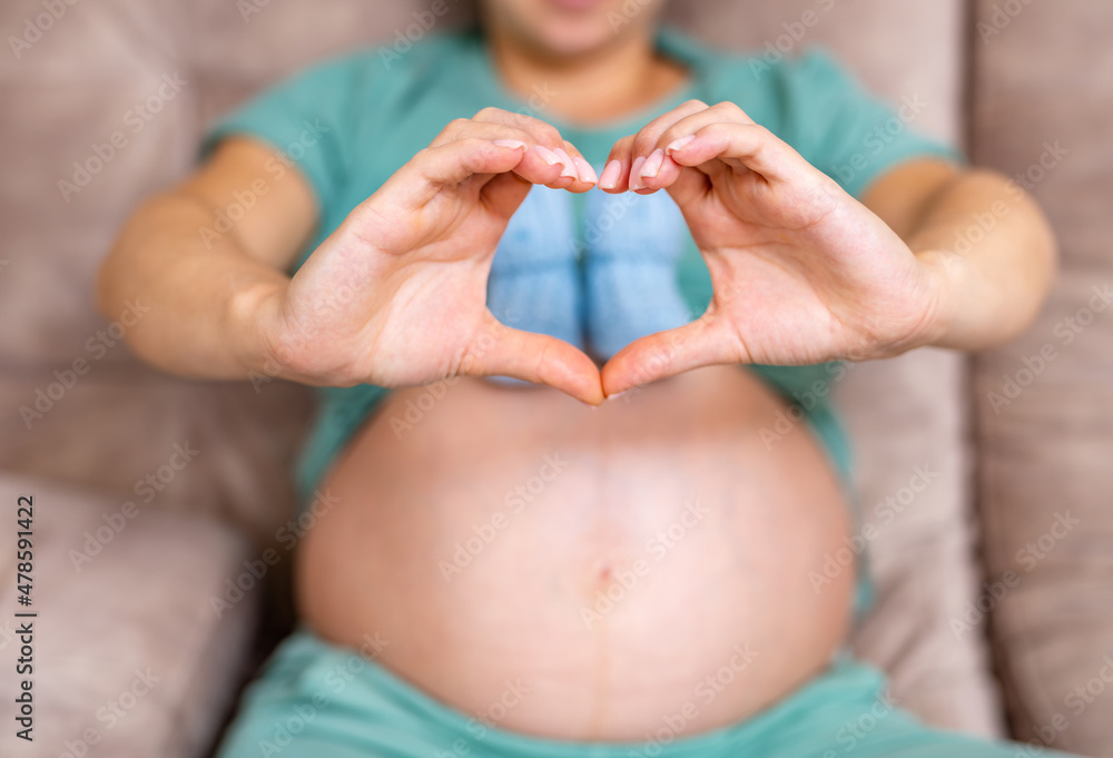 未来的妈妈坐在沙发上，大肚子上抱着婴儿靴。女性为新生儿抱着袜子