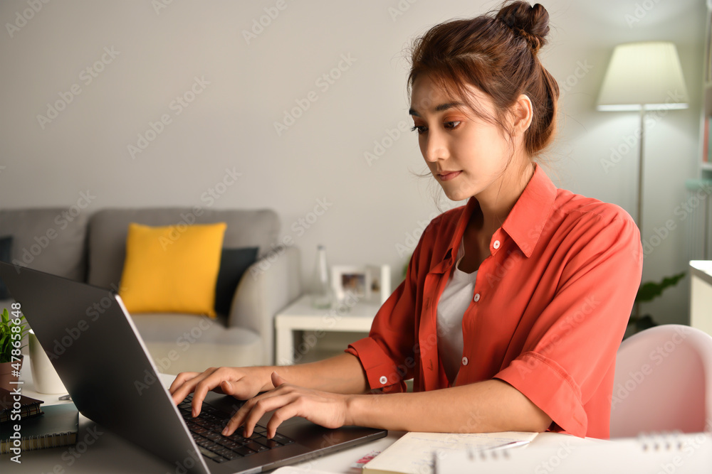 漂亮的亚洲女人在家用笔记本电脑工作。女学生坐在笔记本电脑上在线学习