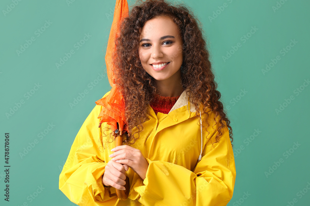 身穿黄色雨衣、绿色背景带伞的年轻非裔美国妇女