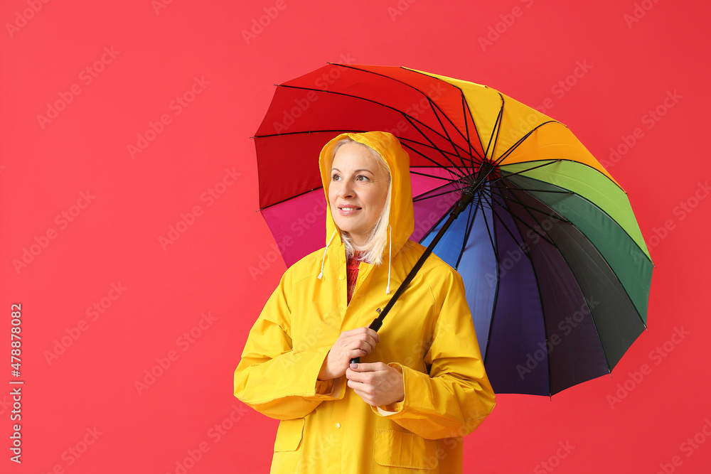 美丽的成熟女人穿着雨衣，颜色背景上带着雨伞