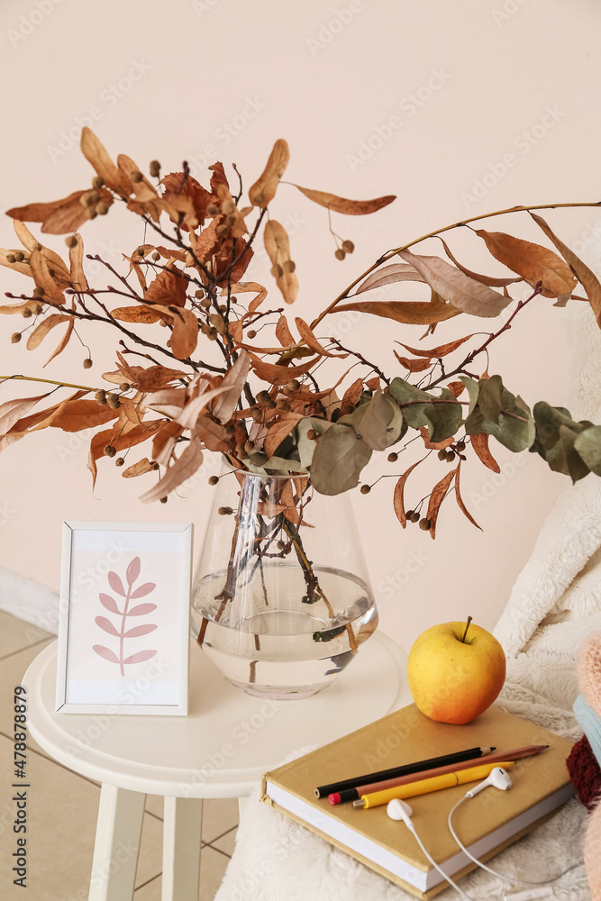 Vase with autumn branches, photo frame, book and earphones near light wall