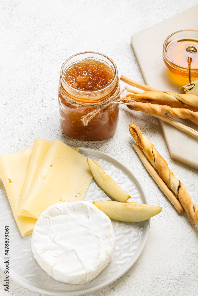 Plate with glass jar of tasty pear jam, cheese and crackers on white background