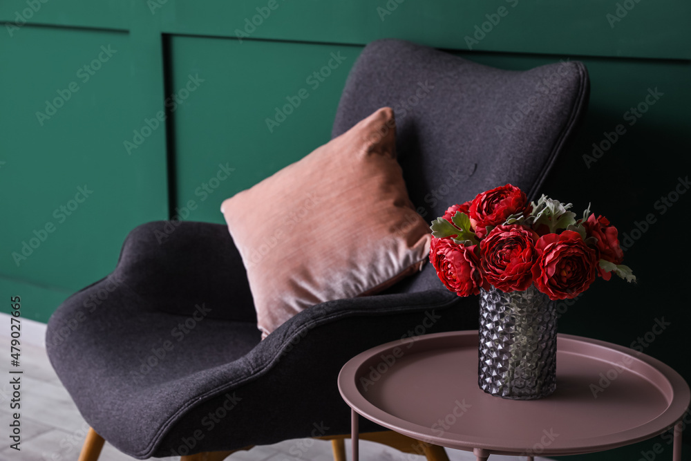 Vase with red peony flowers on coffee table and armchair near green wall