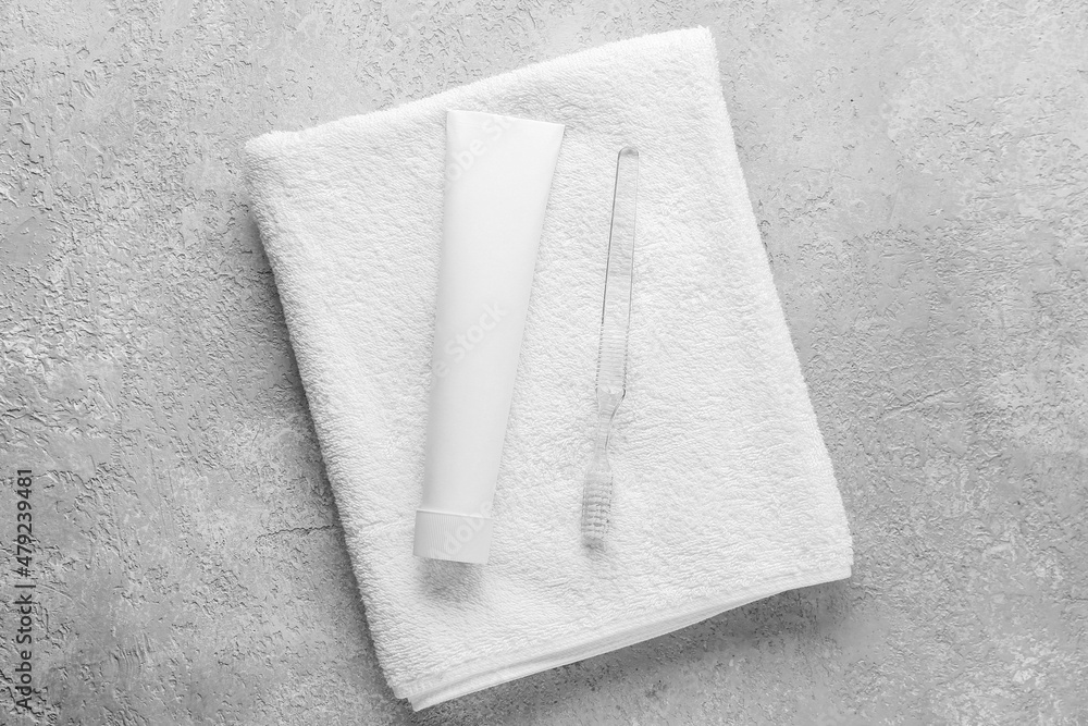 Tube with tooth paste, brush and towel on grey background