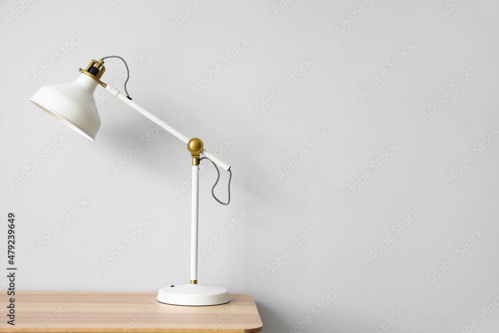 Modern white lamp on wooden table near light wall