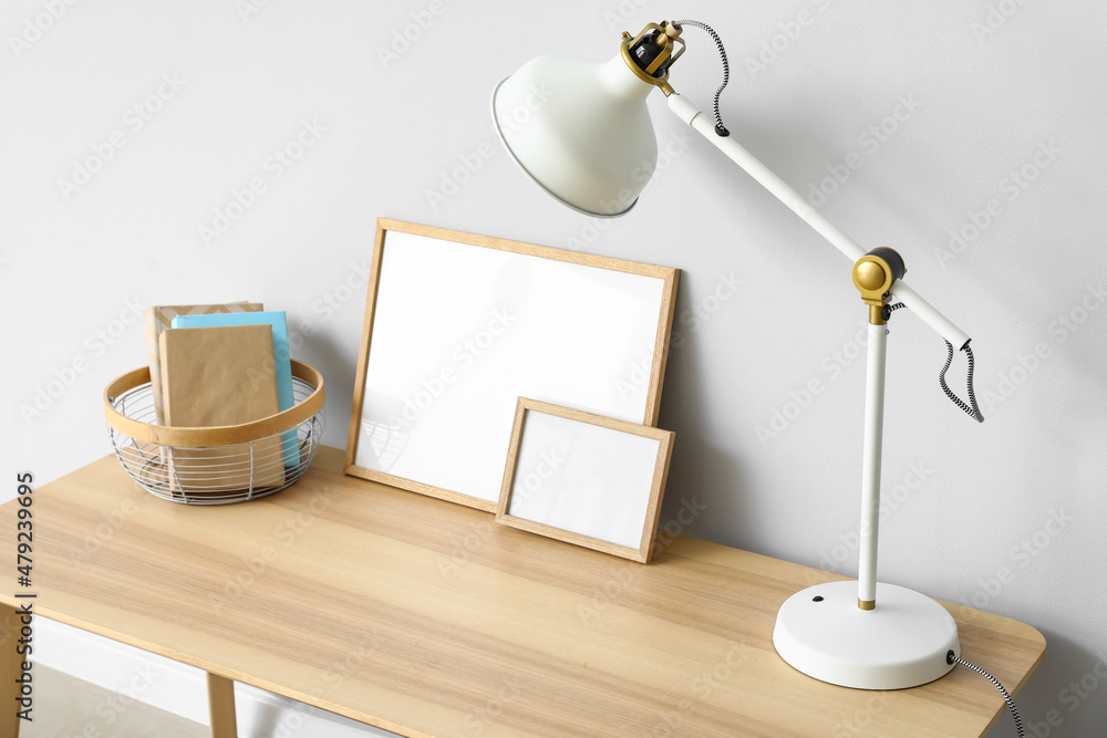 Table with white lamp, books and frames near light wall