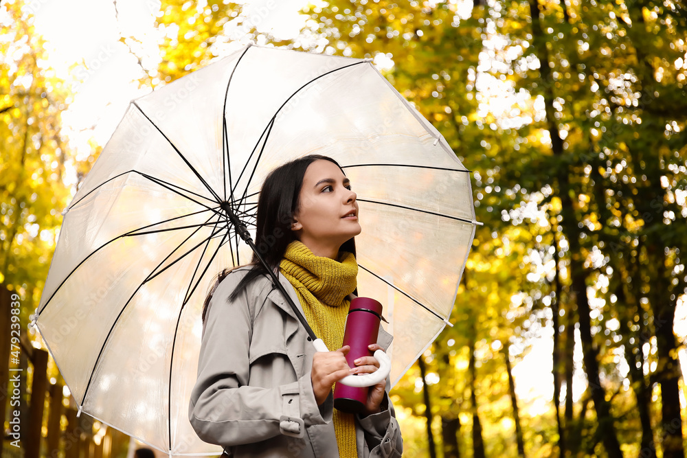 Young woman with umbrella and thermos bottle in autumn forest