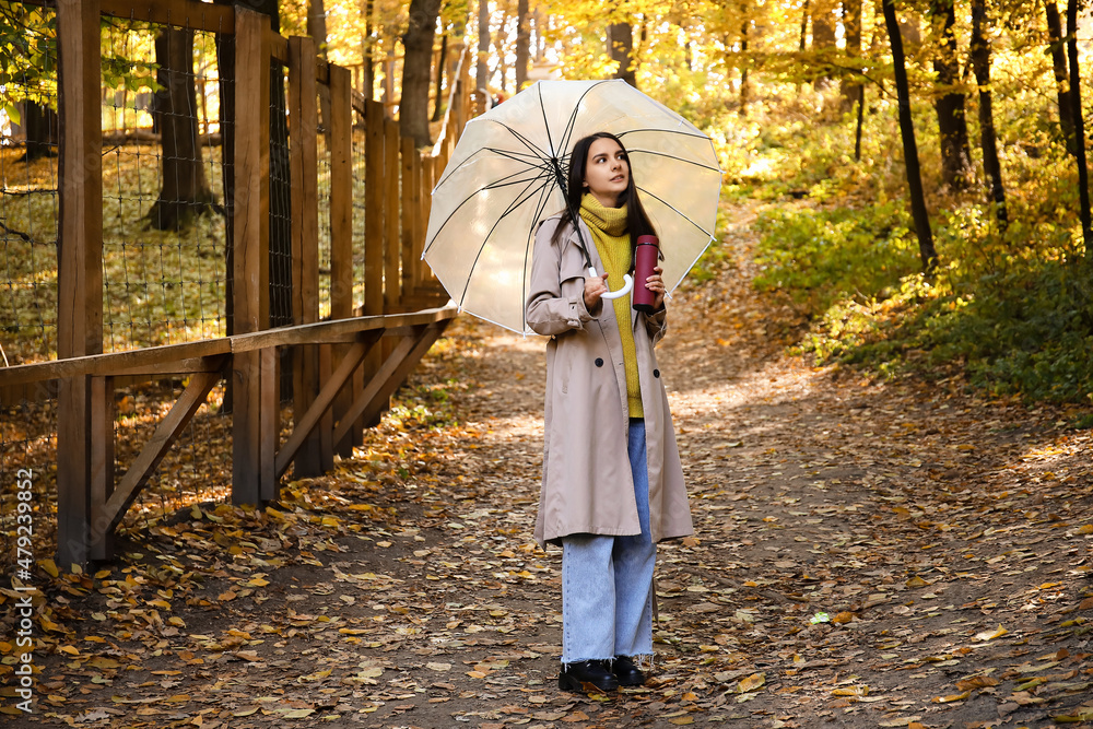 秋天公园里带着雨伞和保温瓶的年轻女子