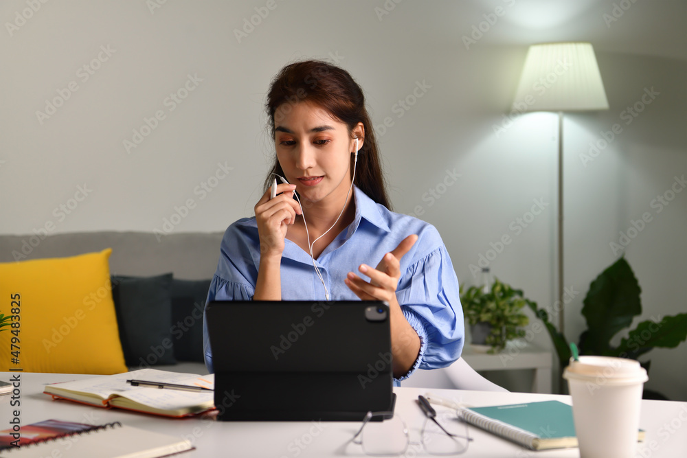 微笑并感觉积极。戴着耳机在平板电脑上视频通话的快乐亚洲女性