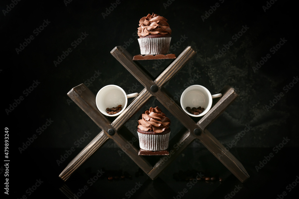 Wooden holder with tasty chocolate cupcakes and cups with coffee beans on dark background