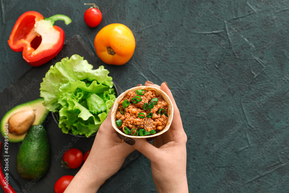 Woman holding tasty burrito on dark background