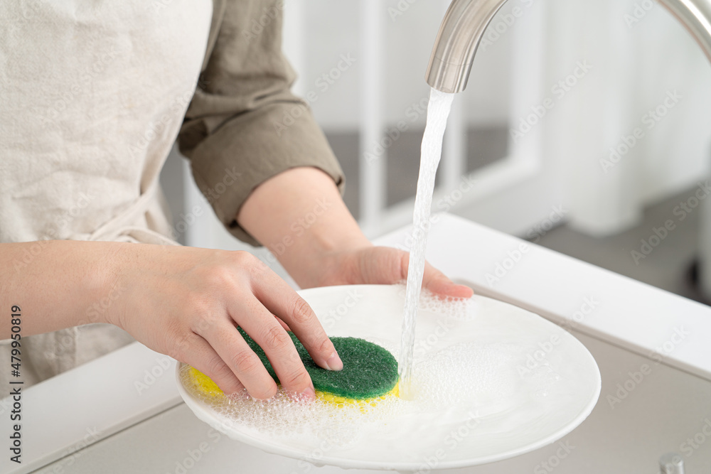 Woman housekeeper is doing the dishes at home kitchen.