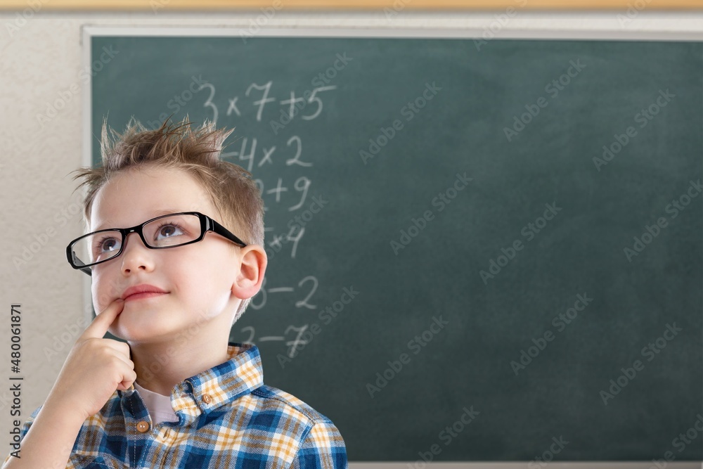 Student child writes with chalk on a blackboard solution of an example in mathematics.