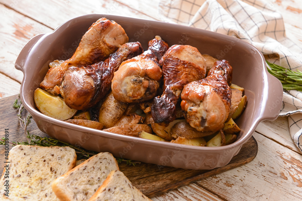 Baking dish with tasty cooked chicken drumsticks and potatoes on table