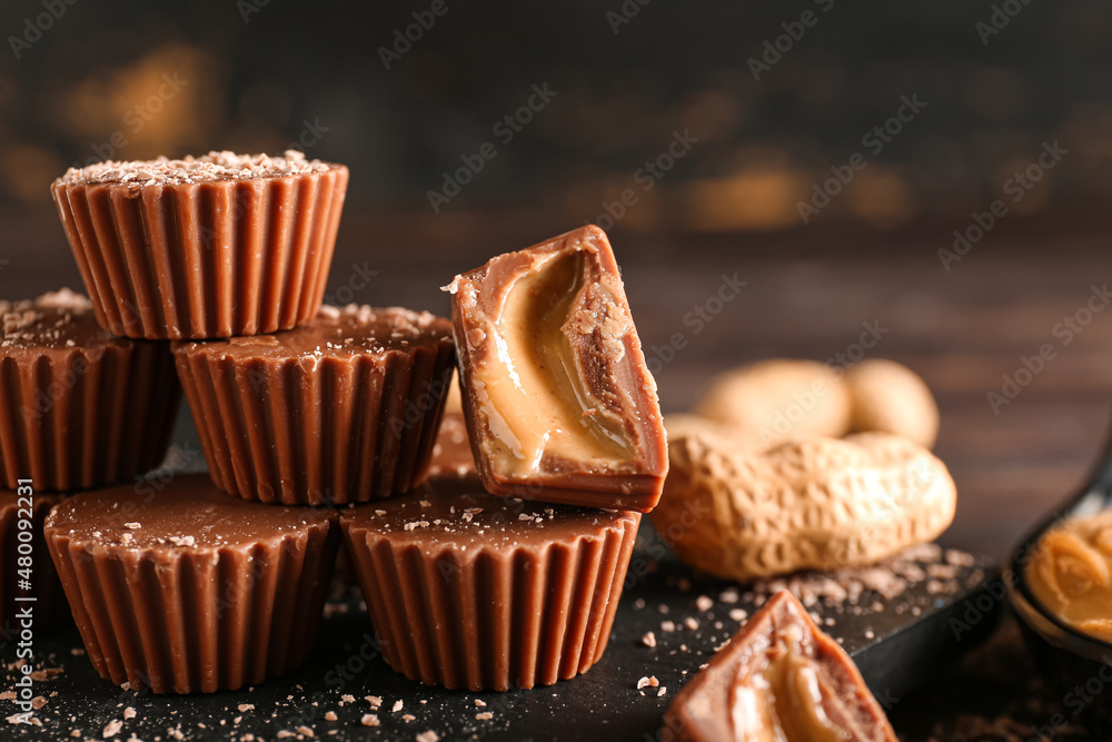 Board with tasty chocolate candies with peanut butter on dark wooden background, closeup