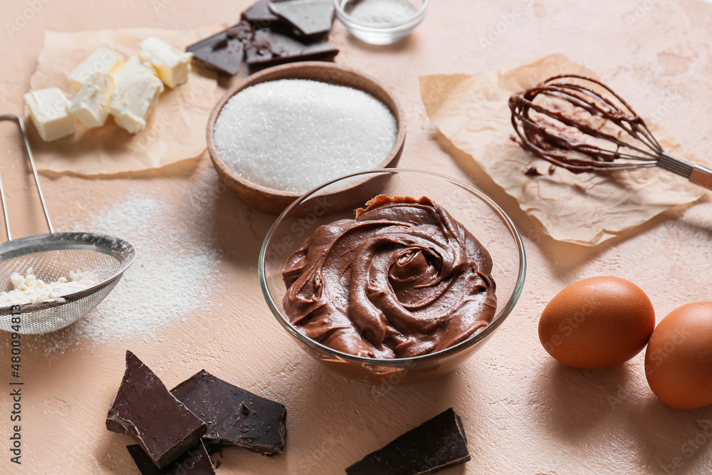 Bowl with fresh dough and ingredients for preparing chocolate brownie on beige background