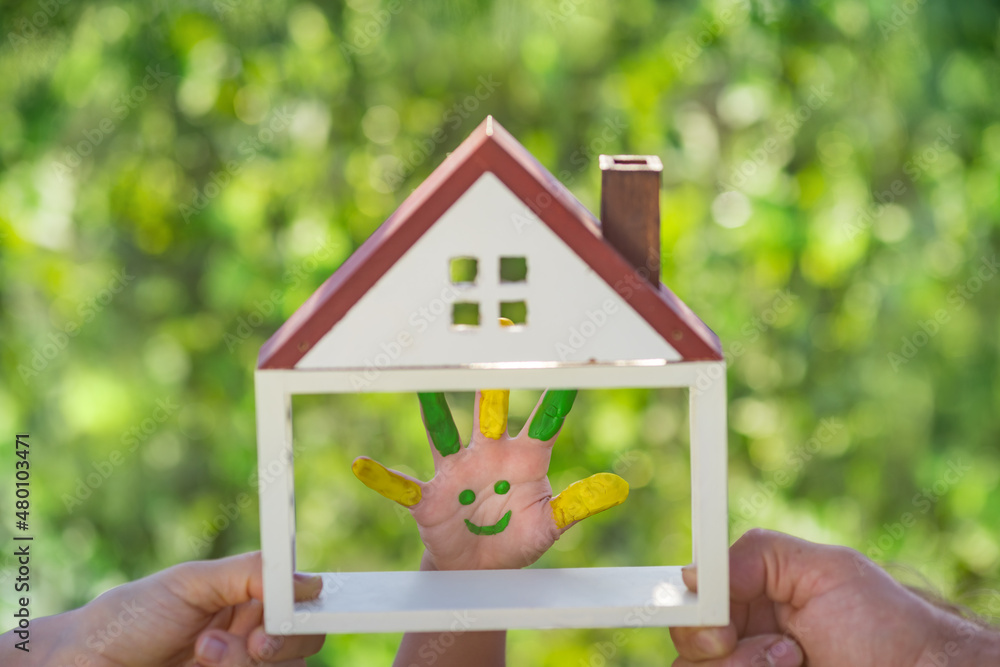 Family holding house in hands against spring green background