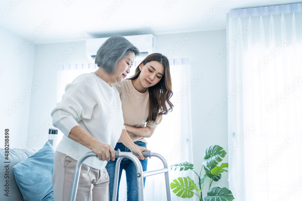 Asian daughter support older woman grandma walk with walker at home. 