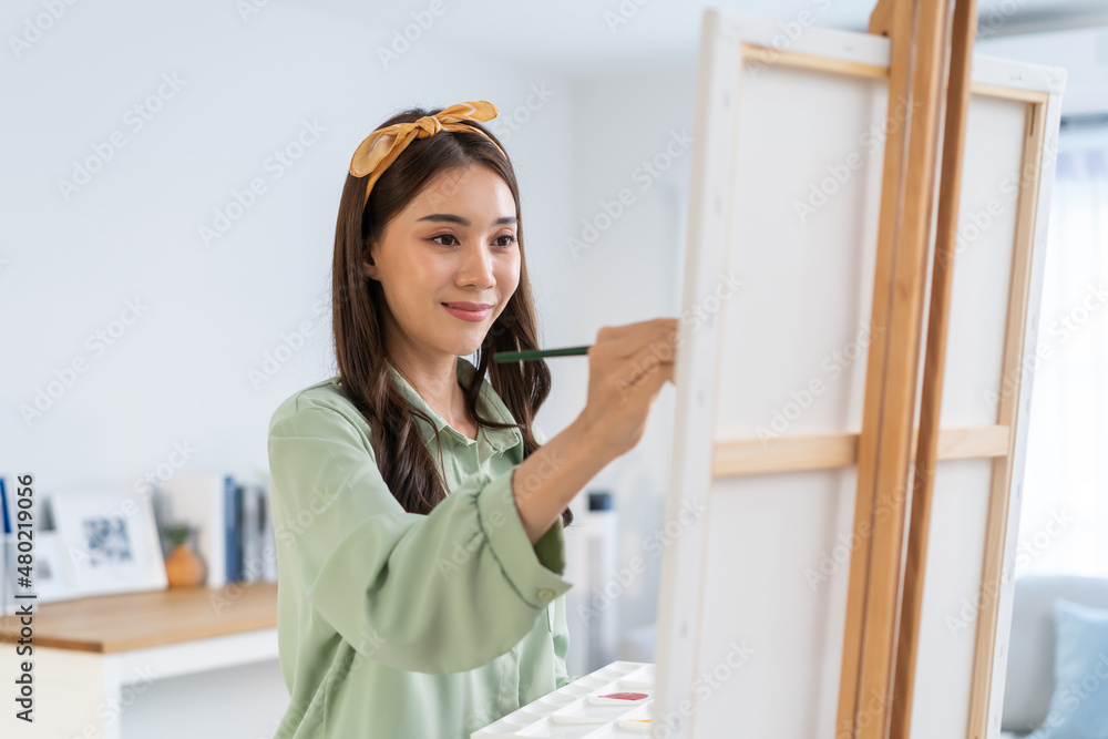 Asian young talented woman artist coloring on painting board in house. 