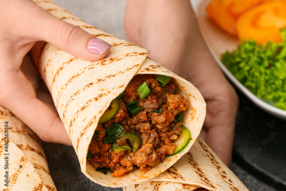 Woman holding tasty burrito at table, closeup